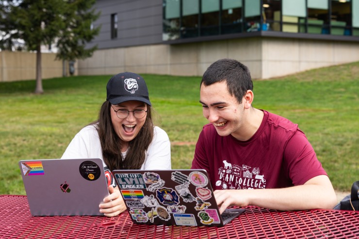 Students reviewing work happily while siting at picnic table 