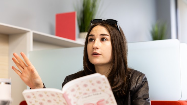 Woman holding a book and having a conversation with someone.